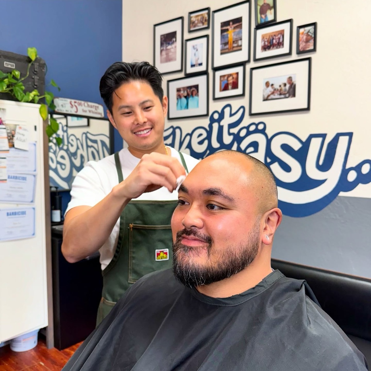 A barber finishing a client’s cut in front of the shop’s “take it easy” wall