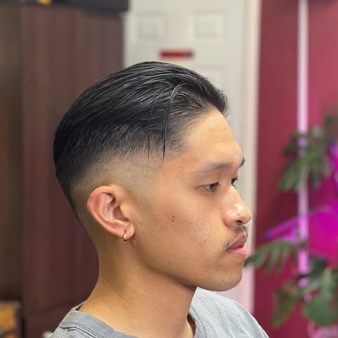 A finished mid fade with the top styled back, seen in profile