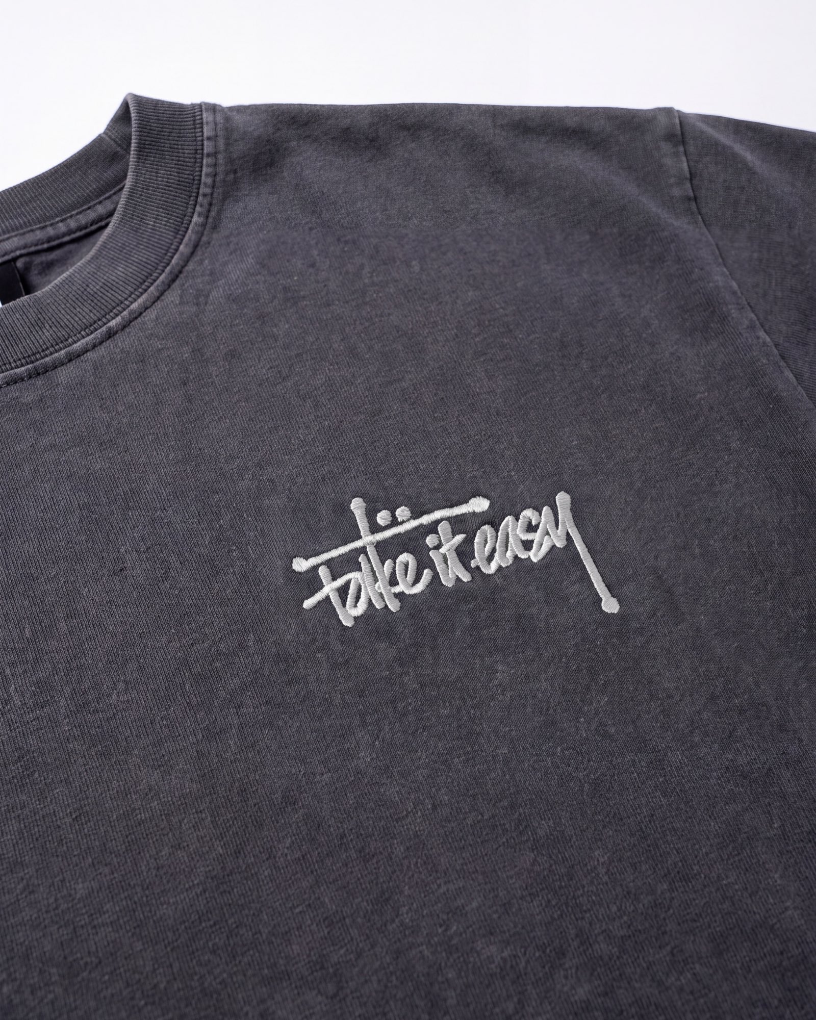 Close-up of the cream embroidered “take it easy” mark on the chest of the charcoal tee