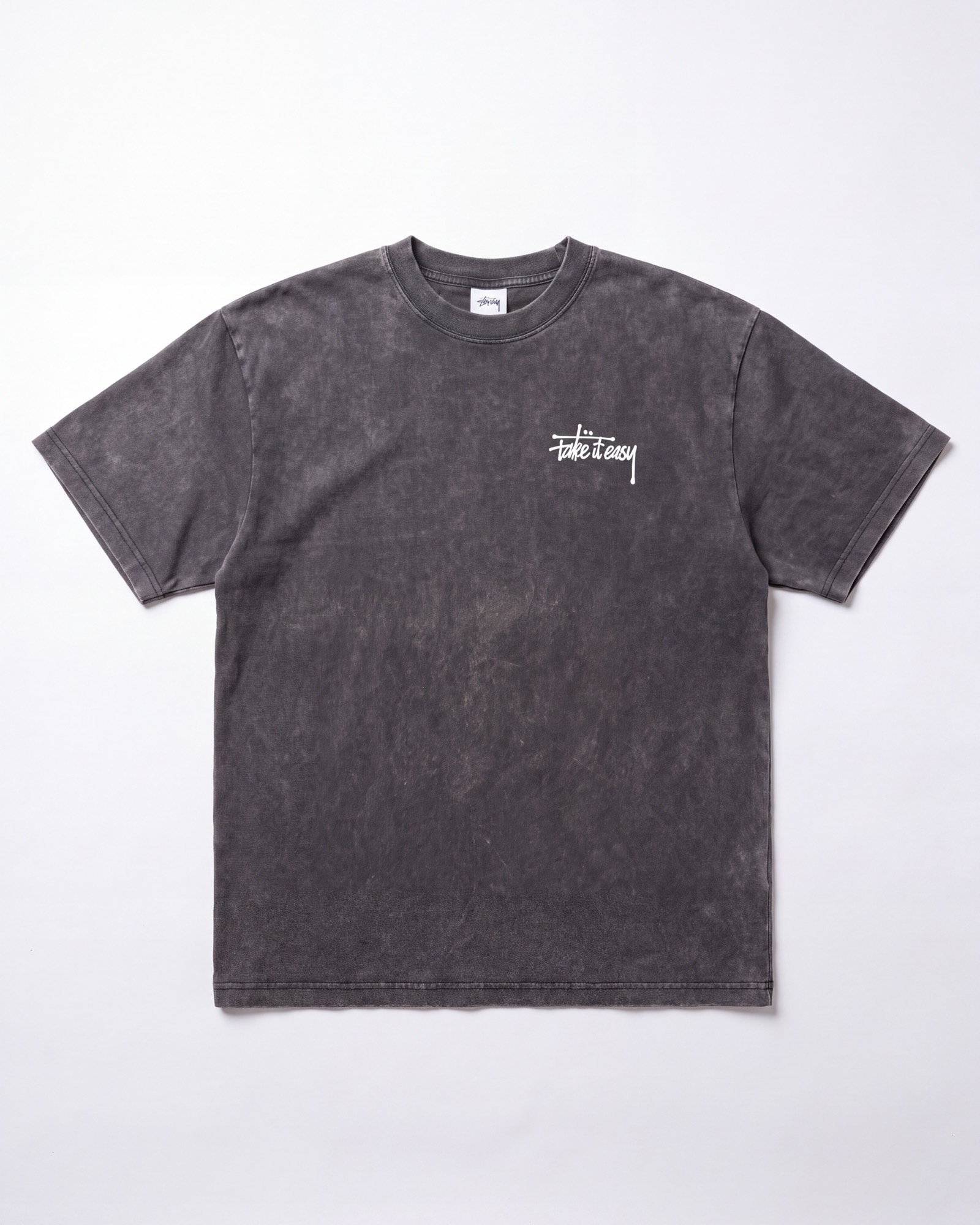The washed charcoal Take It Easy tee laid flat, with the cream hand-lettered mark on the left chest