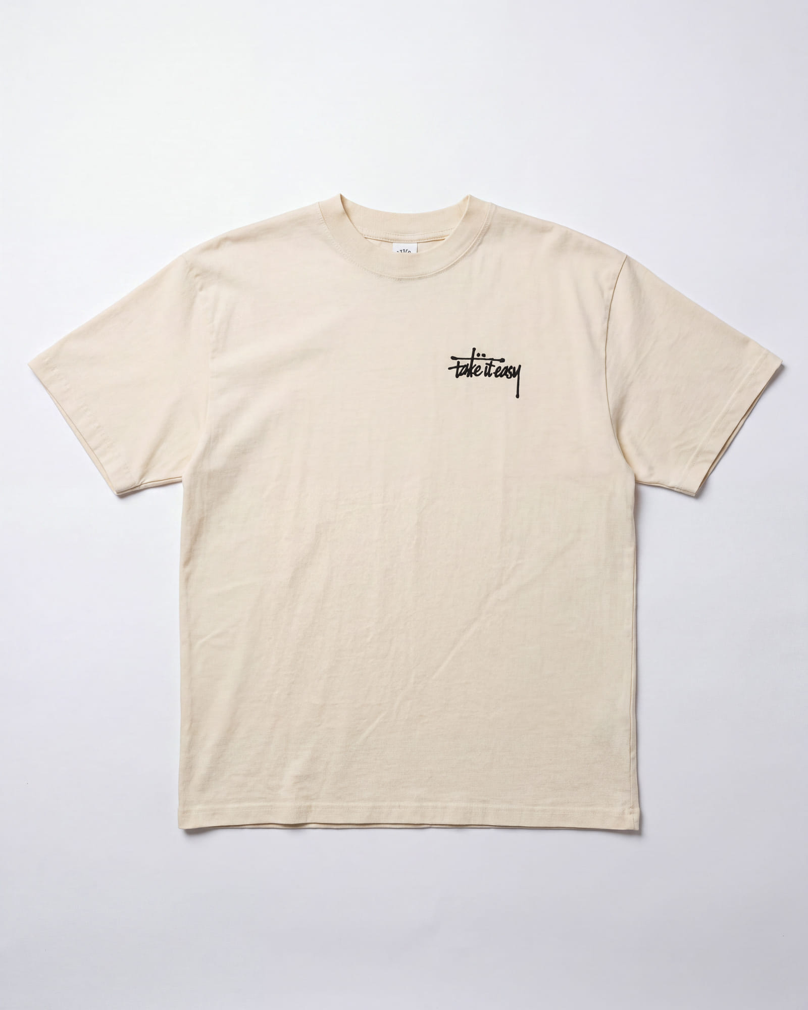 The cream Take It Easy tee laid flat, with the black hand-lettered mark on the left chest