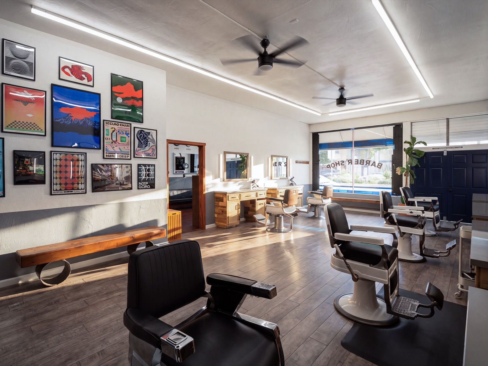 The long room at Juan’s Barbershop, framed prints filling the wall above a wooden bench